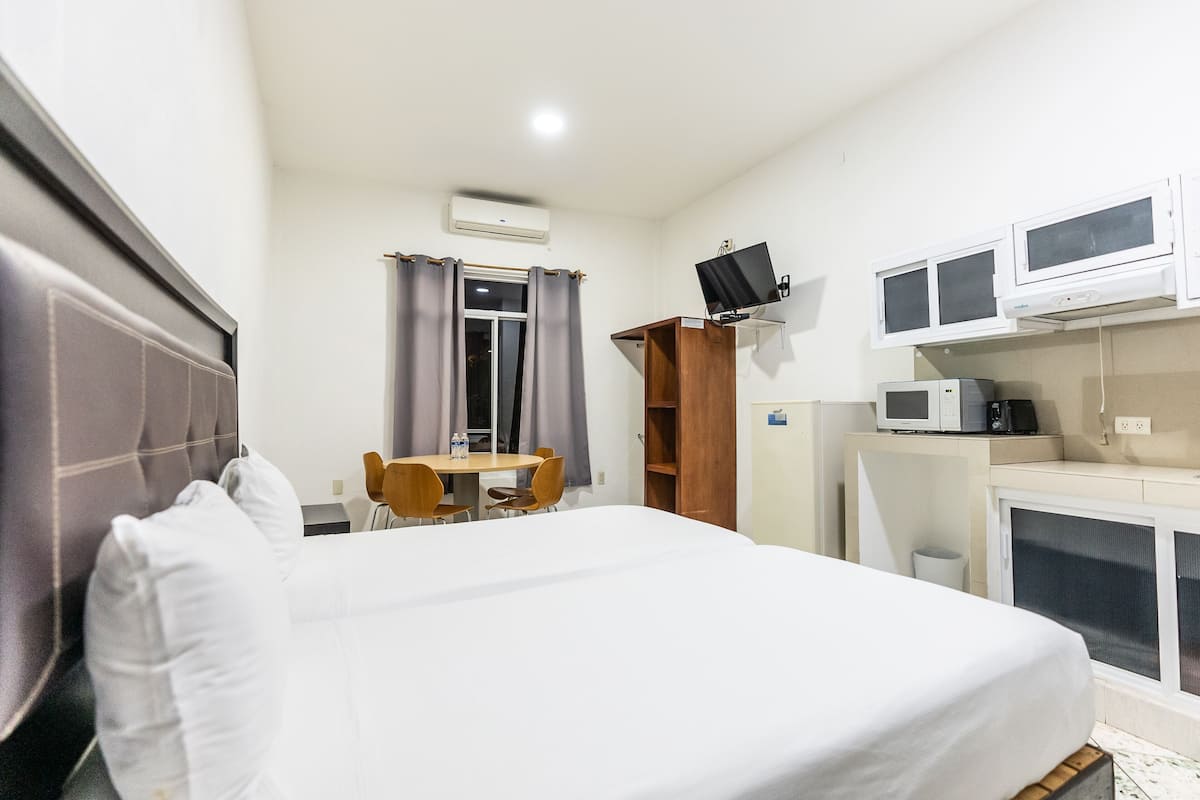 Een hotelkamer met een bed, bureau, stoel, televisie en kitchenette.