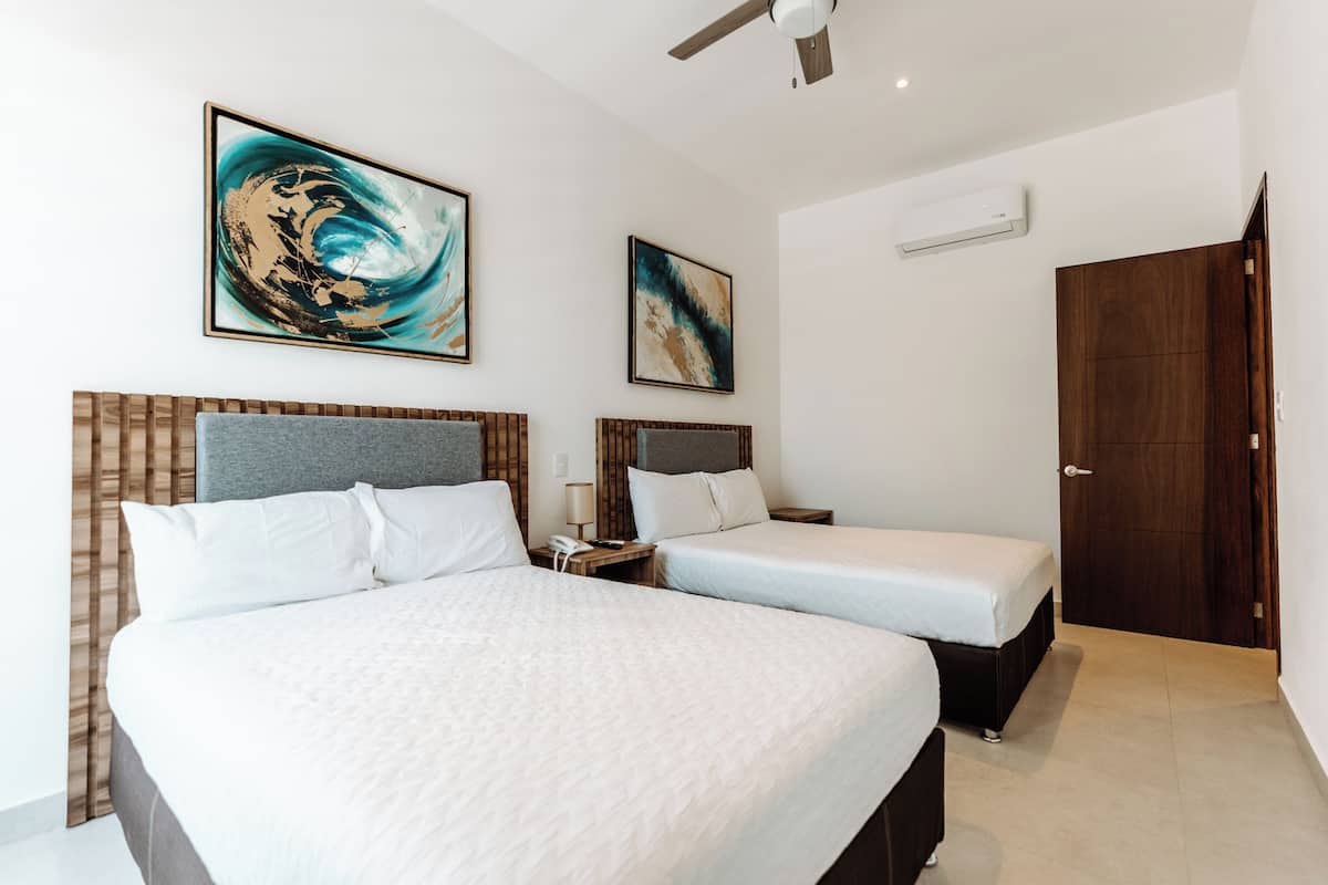 Een hotelkamer met twee bedden, een houten hoofdbord, een plafondventilator en twee ingelijste kunstwerken aan de muur.