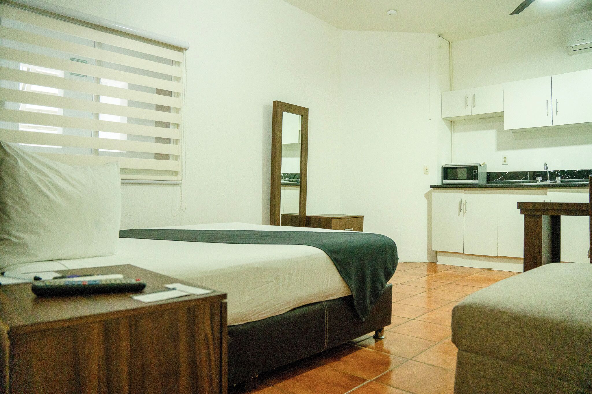 Quarto com cama, mesa de cabeceira e uma pequena cozinha compacta.