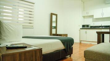 Quarto com cama, mesa de cabeceira e uma pequena cozinha compacta.