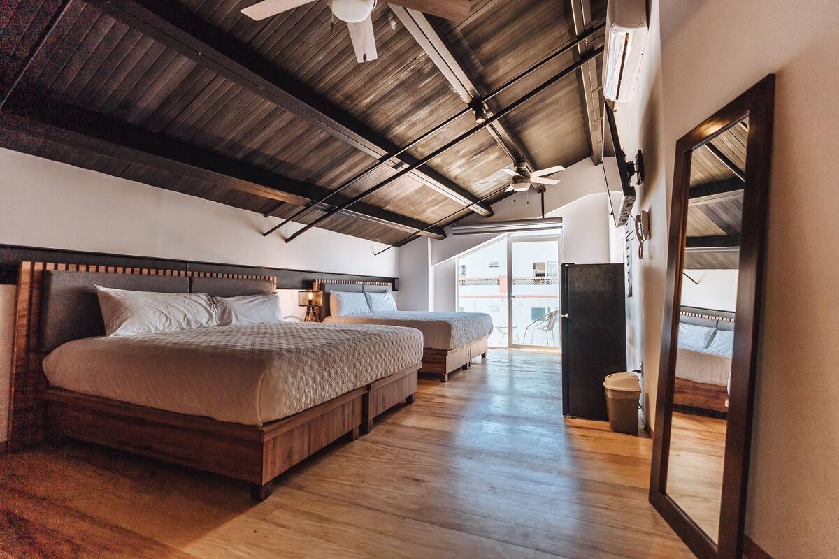Een slaapkamer met twee bedden, houten vloeren, een plafondventilator en een grote spiegel.