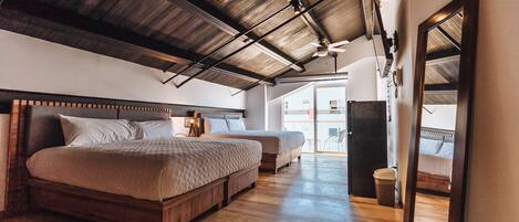 A bedroom with two beds, wooden flooring, a ceiling fan, and a large mirror.