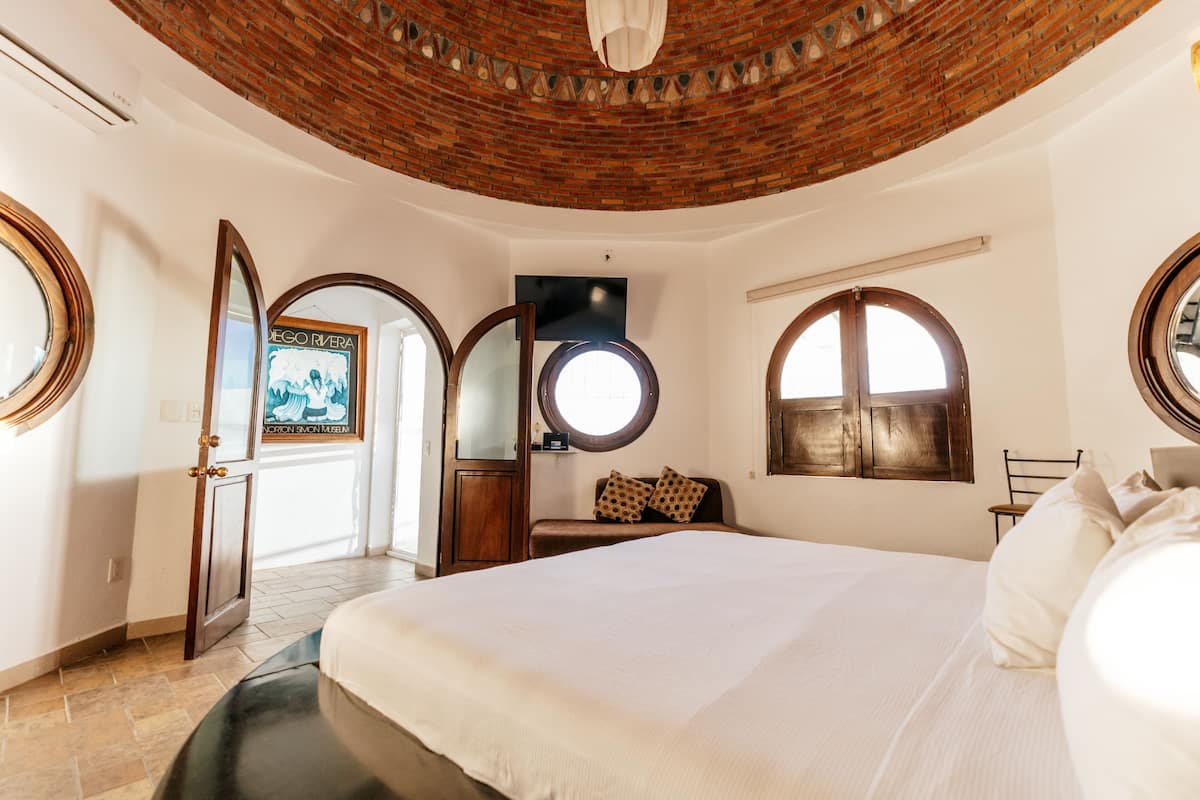 Een slaapkamer met een groot bed, een houten plafond en een rond raam.