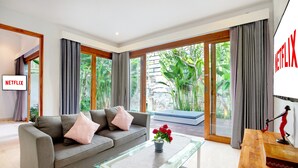 Una sala de estar moderna con un sofá gris, una mesa de centro de vidrio y un ventanal con cortinas.