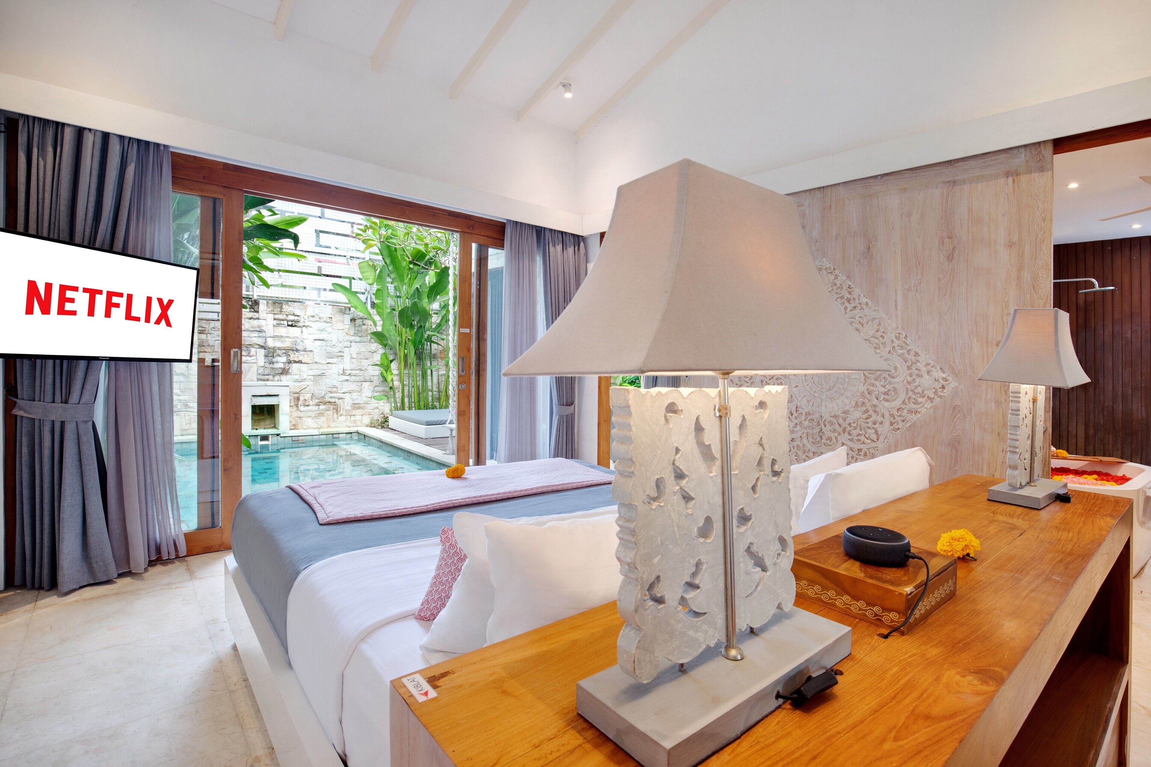 Ein modernes Hotelzimmer mit Bett, Schreibtisch aus Holz, Lampe und Blick auf einen Außenpool.