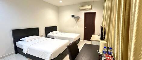 A hotel room with two beds, a desk with a lamp, a chair, and a small table with water bottles and snacks.