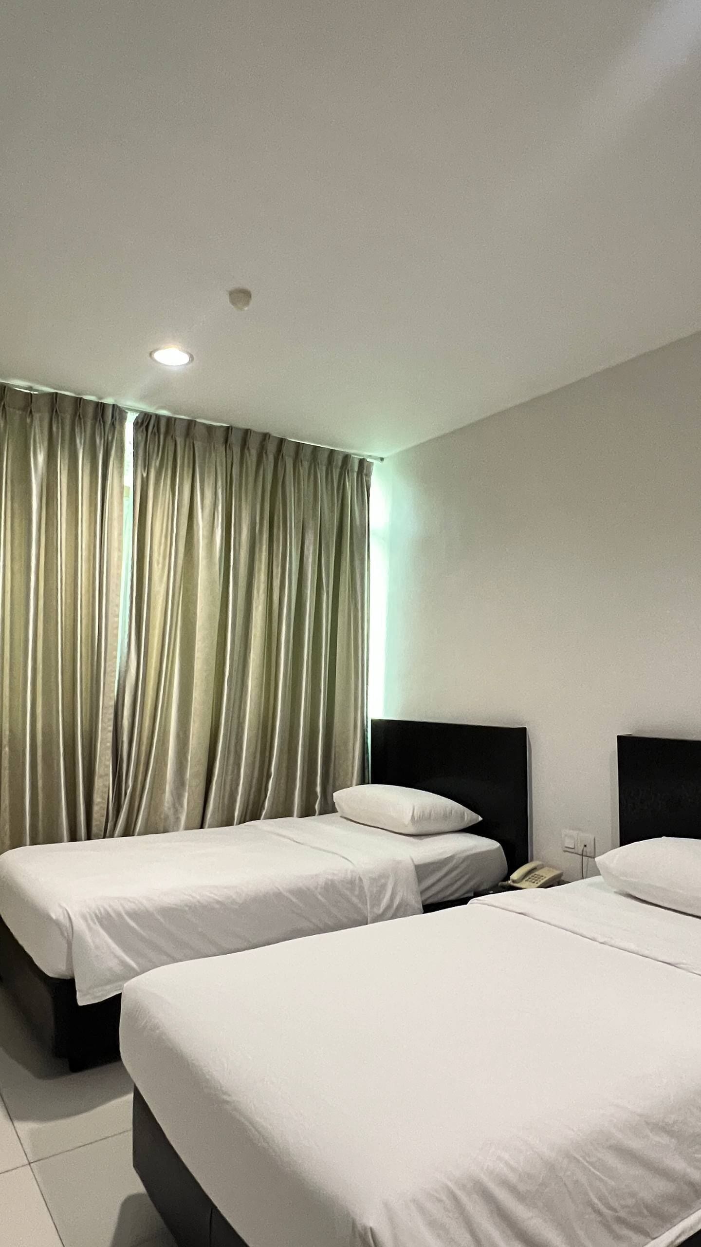 A hotel room with two beds, a telephone, and a curtain.