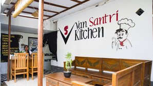 Interior de un restaurante con un banco de madera, una planta en maceta y una pared con el nombre 'Van Santri Kitchen'.