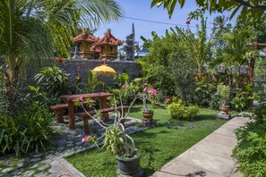 A garden with a wooden bench, potted plants, and a traditional building in the background. - Van Santri Homestay Pemuteran (Pemuteran)