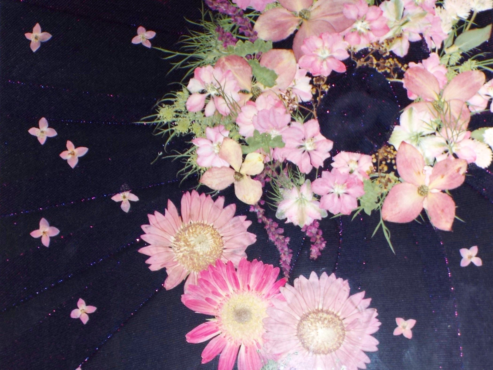 Tecido escuro com flores cor-de-rosa e folhagem verde espalhadas.