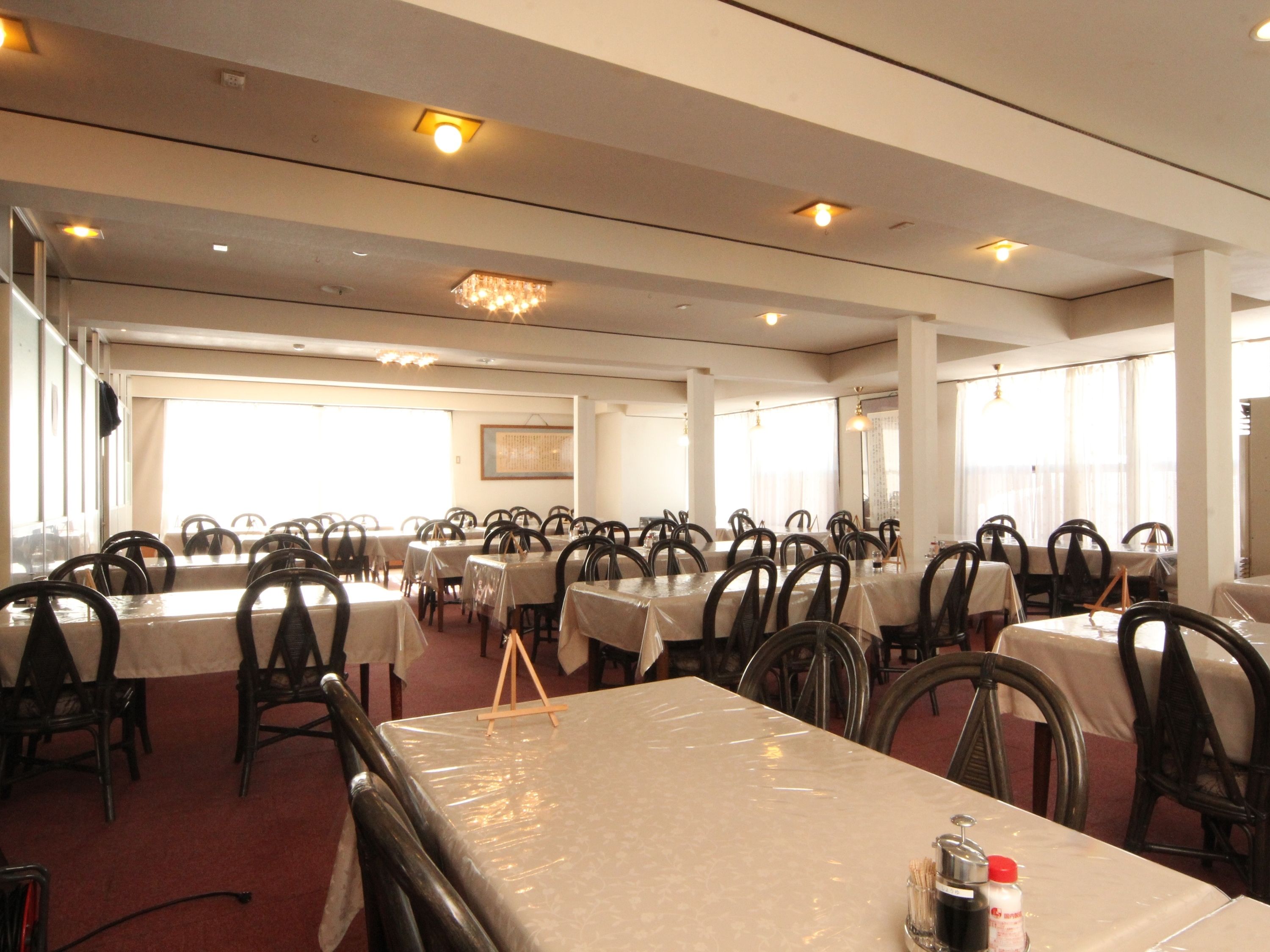 A large dining hall with multiple tables and chairs, arranged in rows.