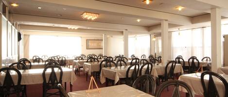 A large dining hall with multiple tables and chairs, arranged in rows.