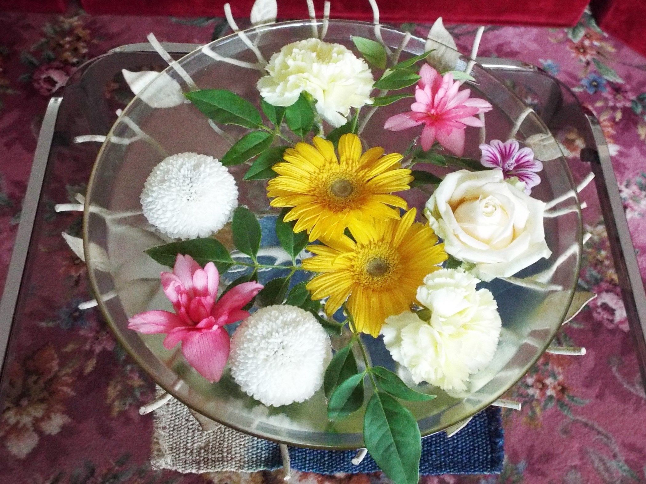 Un florero de vidrio transparente con un arreglo floral que contiene flores amarillas y blancas, una flor rosa y una rosa blanca.