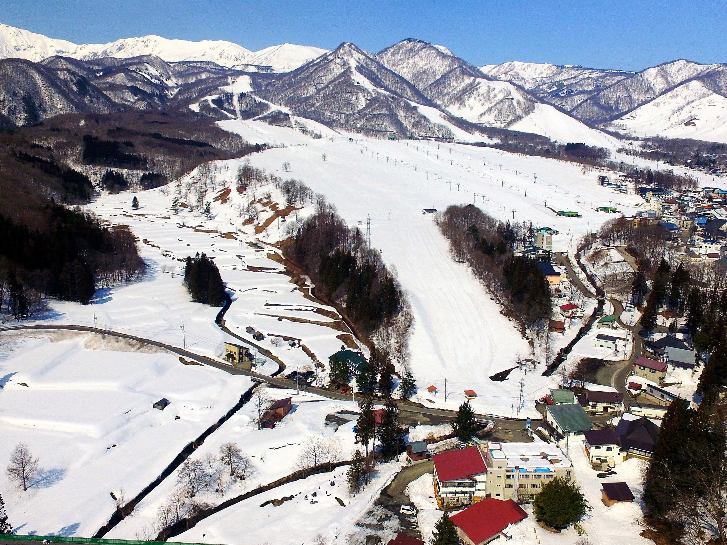 A snow-covered mountain village with a ski slope, buildings, and a clear sky.