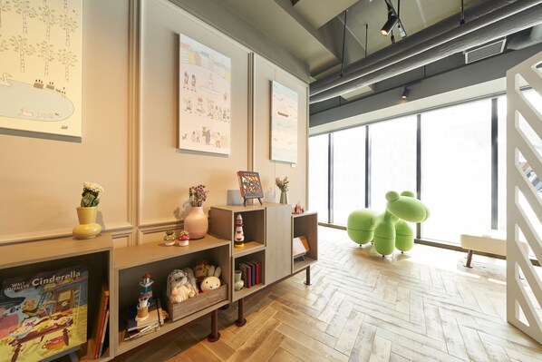 A modern interior with wooden flooring, a large window with a view, and a green frog-shaped chair.