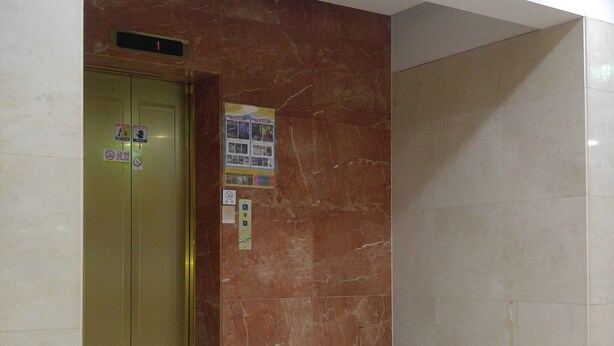 A hallway with a marble wall, an elevator, and a tiled floor. - Odyssey  Hotel (Chungju)