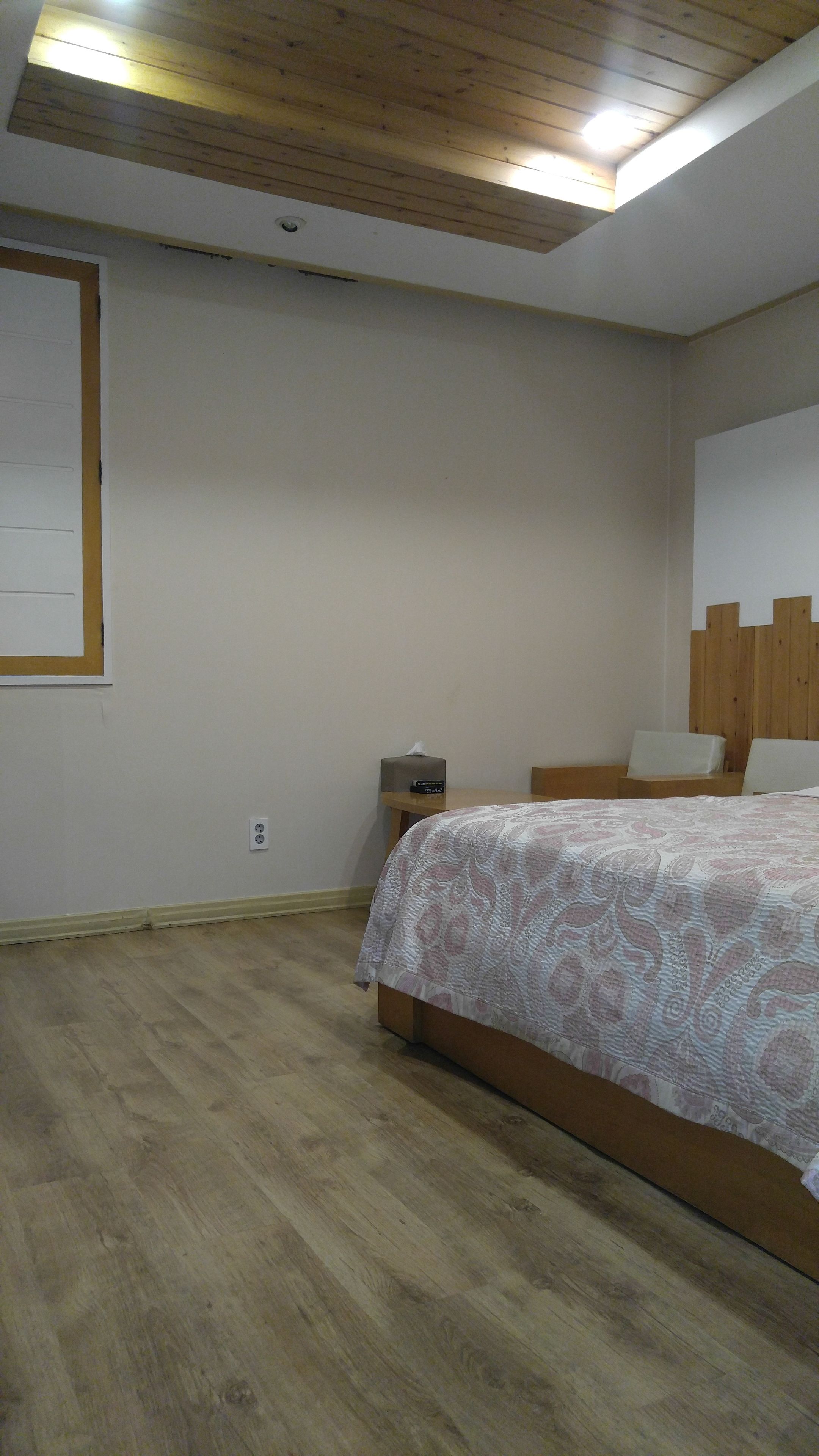Een slaapkamer met een houten vloer, een bed met een geborduurd beddegoed, een nachtkastje met een lamp en een houten hoofdbord.