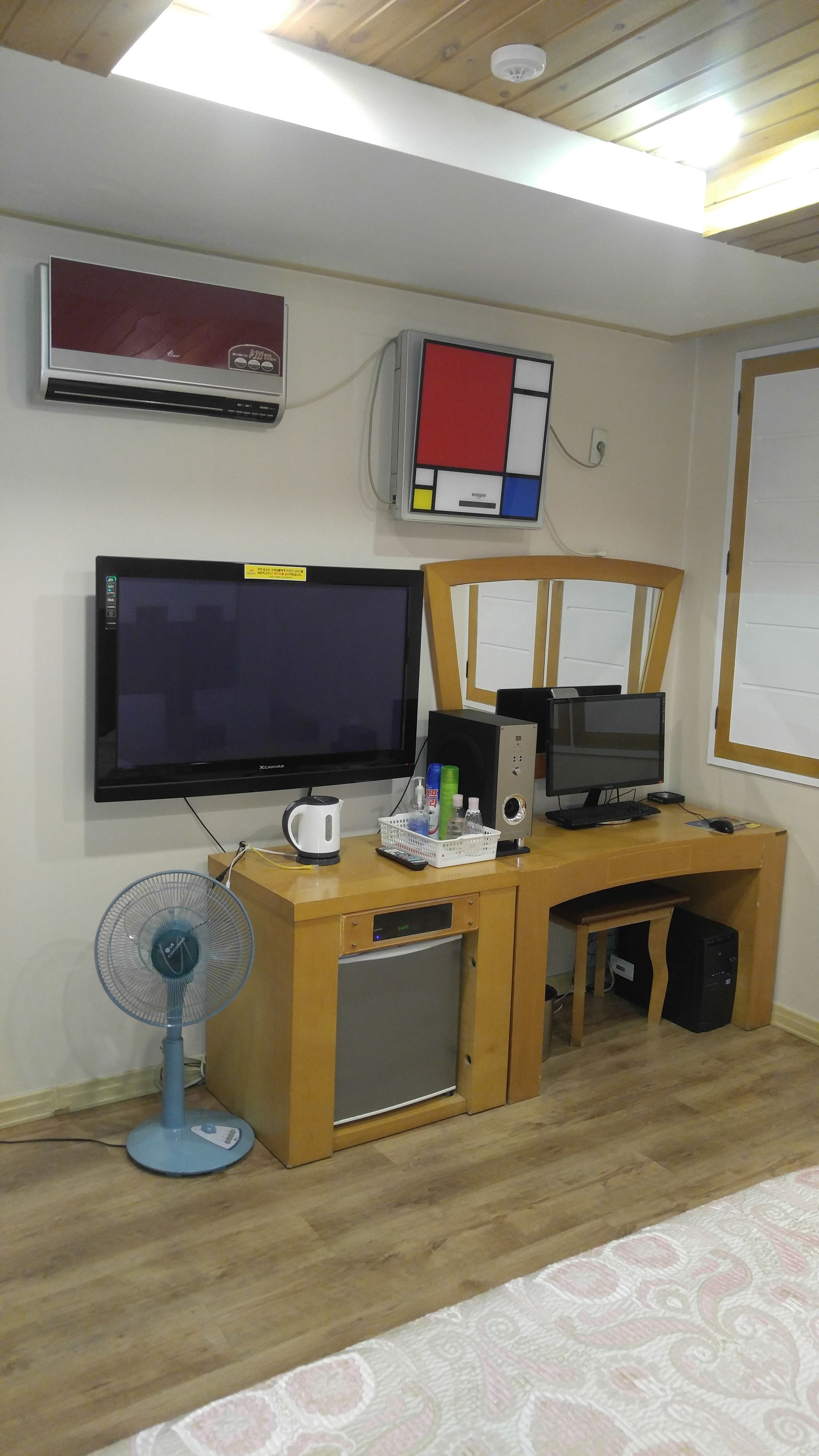 Una oficina en casa con un escritorio, dos monitores, una computadora, un ventilador y aire acondicionado.