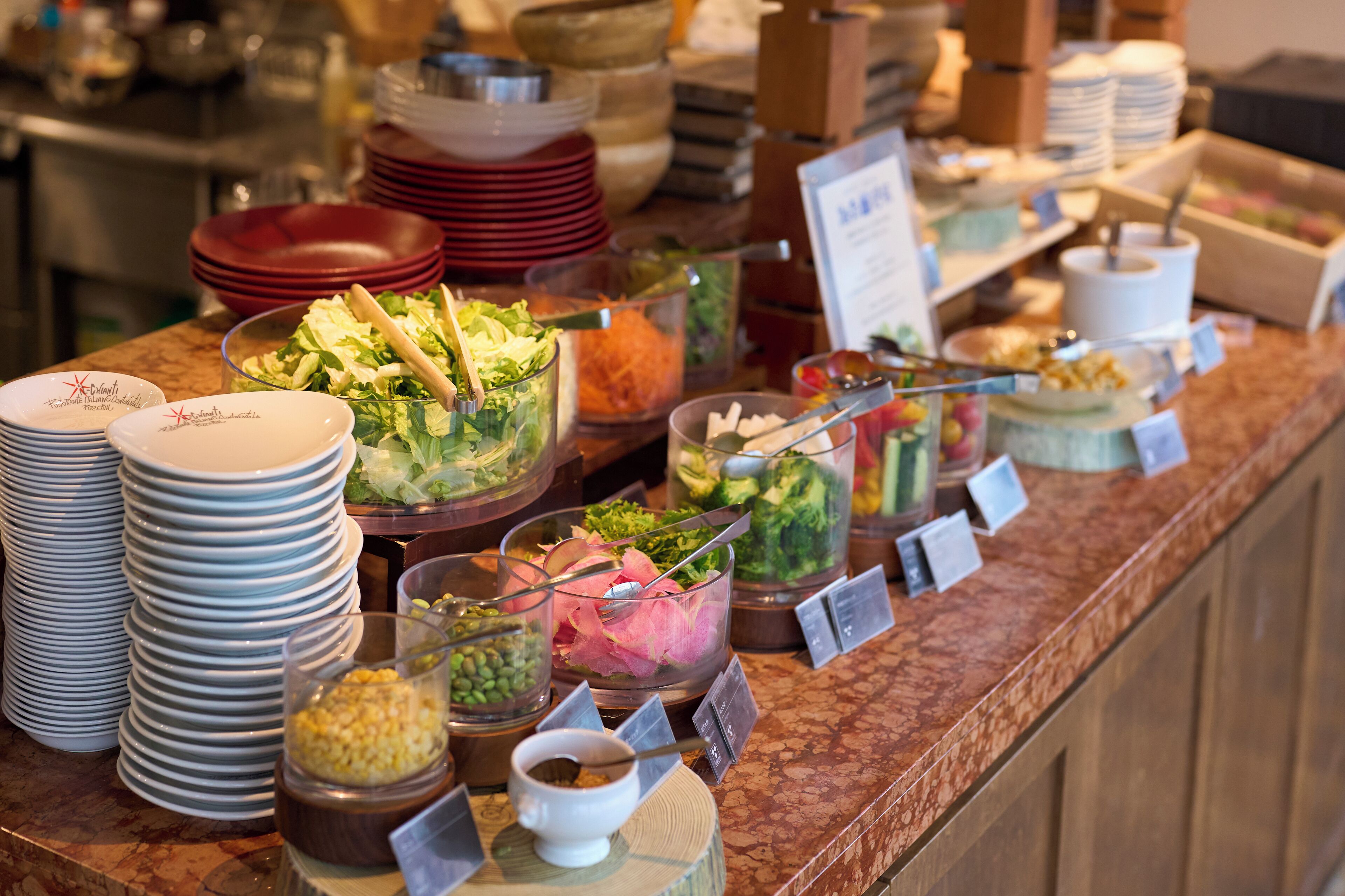 A buffet with various food items and stacked plates.