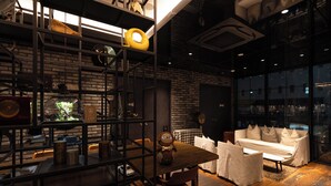 A cozy interior with a brick wall, wooden furniture, and a large window offering a view of the city. - Hotel Resol Akihabara (Tokyo)