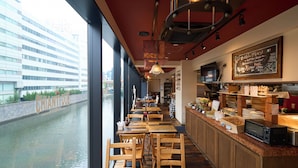 A restaurant with a view of a canal, wooden tables and chairs, a chalkboard menu, and a kitchen area. - Hotel Resol Akihabara (Tokyo)