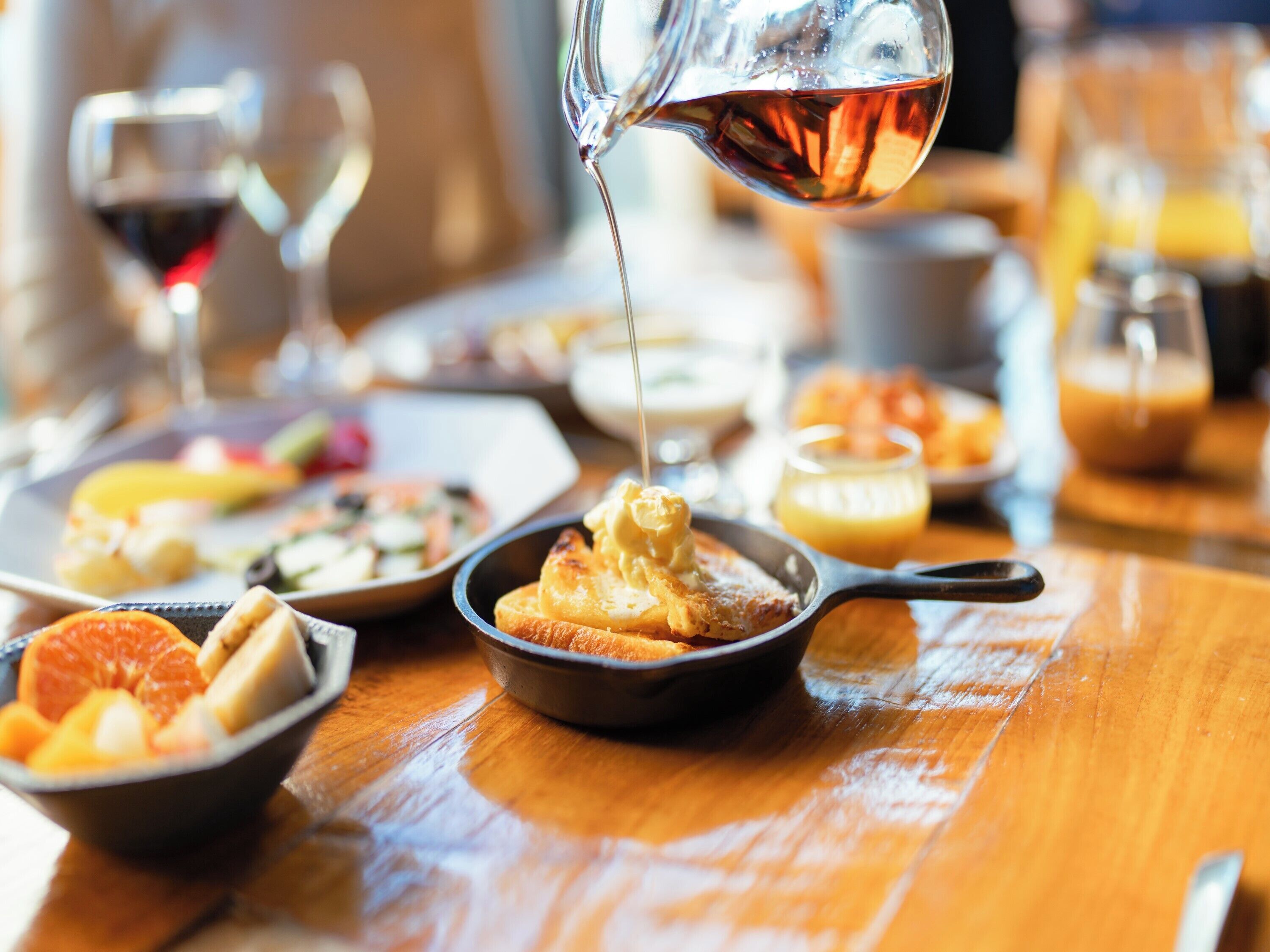 A breakfast setting with a variety of dishes, including toast with butter, fruit, and a bowl of orange juice.