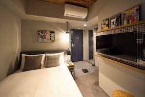 Una camera d'albergo con un letto, un comodino, una TV a parete e una porta che dà su un'altra stanza.