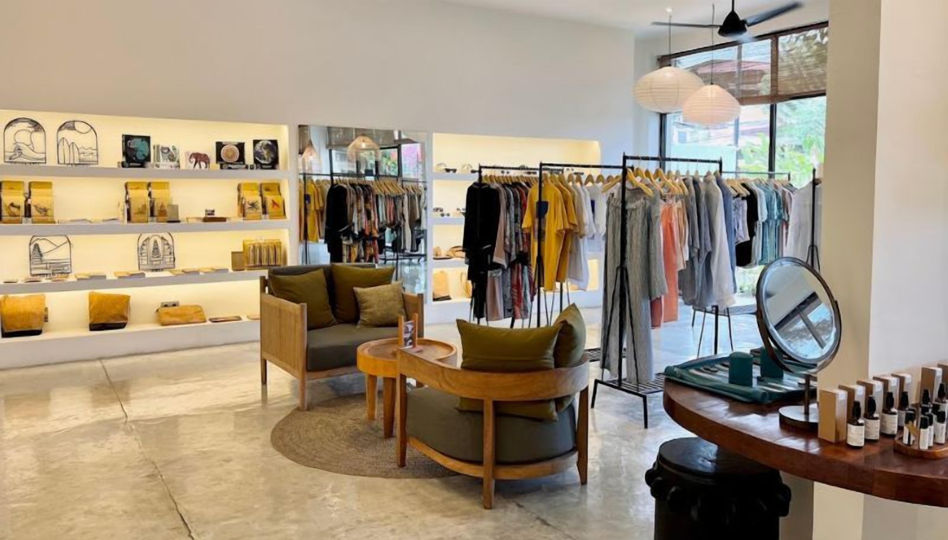 Een modern interieur met een zithoek, kledingrekken en een presentatie van spullen op planken.