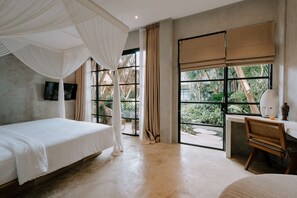 A bedroom with a bed, a desk, and a window with a view of greenery.