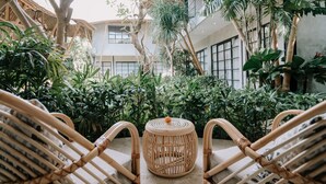 Une cour avec des chaises en osier, une table ronde au centre et une végétation tropicale luxuriante.
