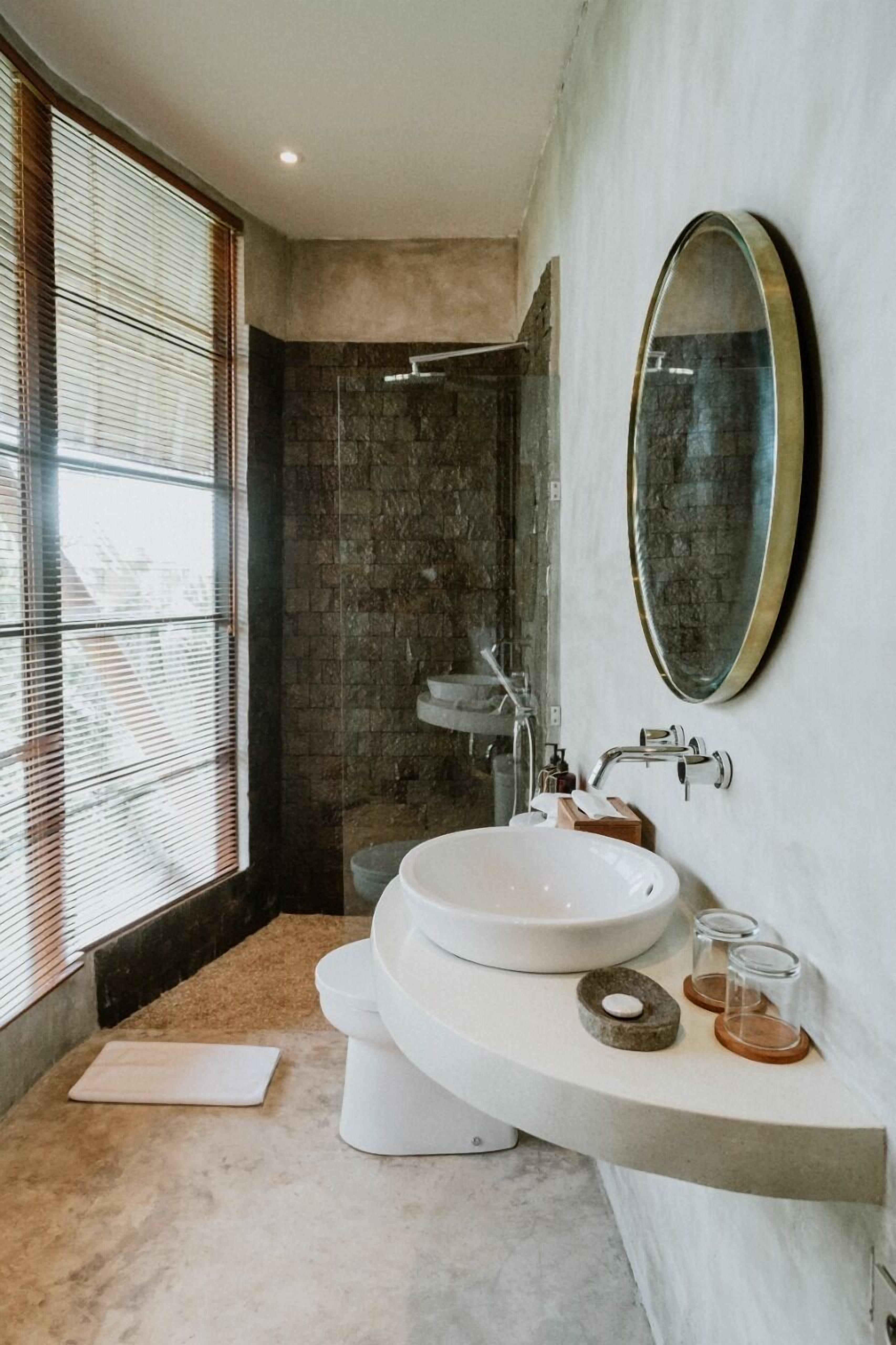 A modern bathroom with a large oval mirror, a white sink, and a shower area.