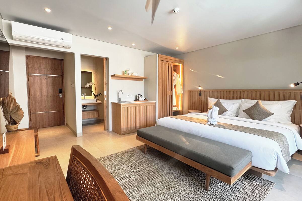 Une chambre d’hôtel moderne équipée d’un grand lit, d’un bureau, d’une petite kitchenette et d’une salle de bain.