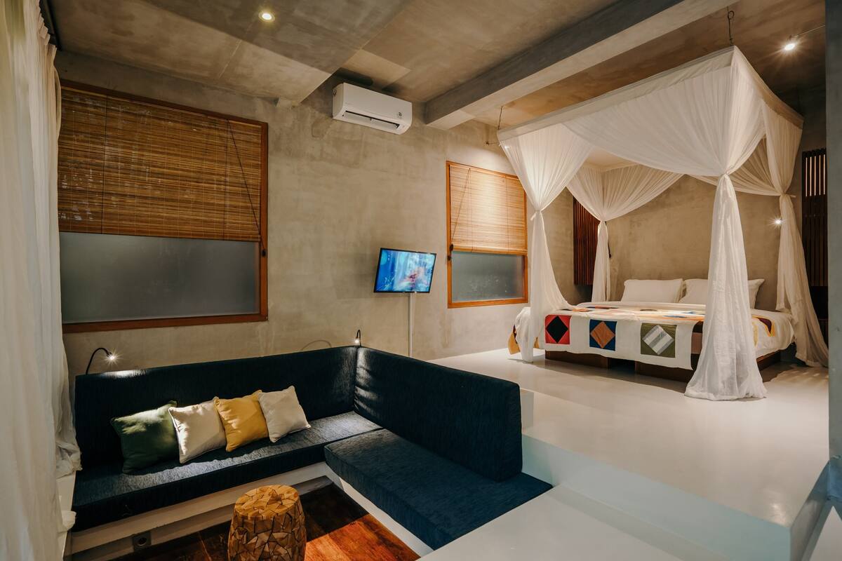 Une chambre à coucher avec un canapé bleu foncé, un lit à baldaquin blanc, une télévision et un climatiseur fixé au mur.