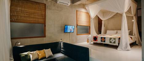 A bedroom with a dark blue sofa, a white canopy bed, a television, and a wall-mounted air conditioner.