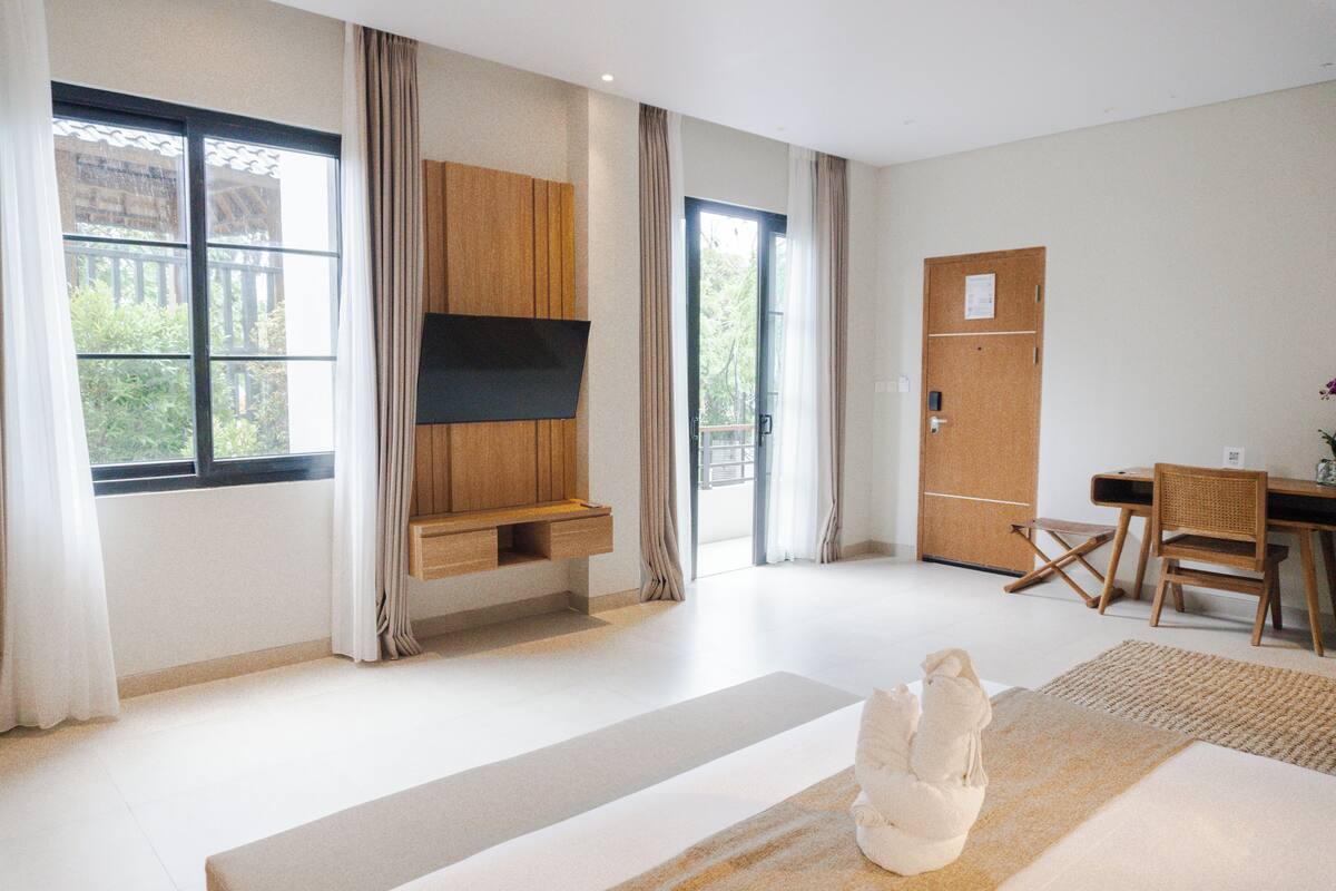 Ett modernt hotellrum med ett stort fönster, en platt-TV som är monterad på en träpanel, ett skrivbord med en stol och en liten matta.