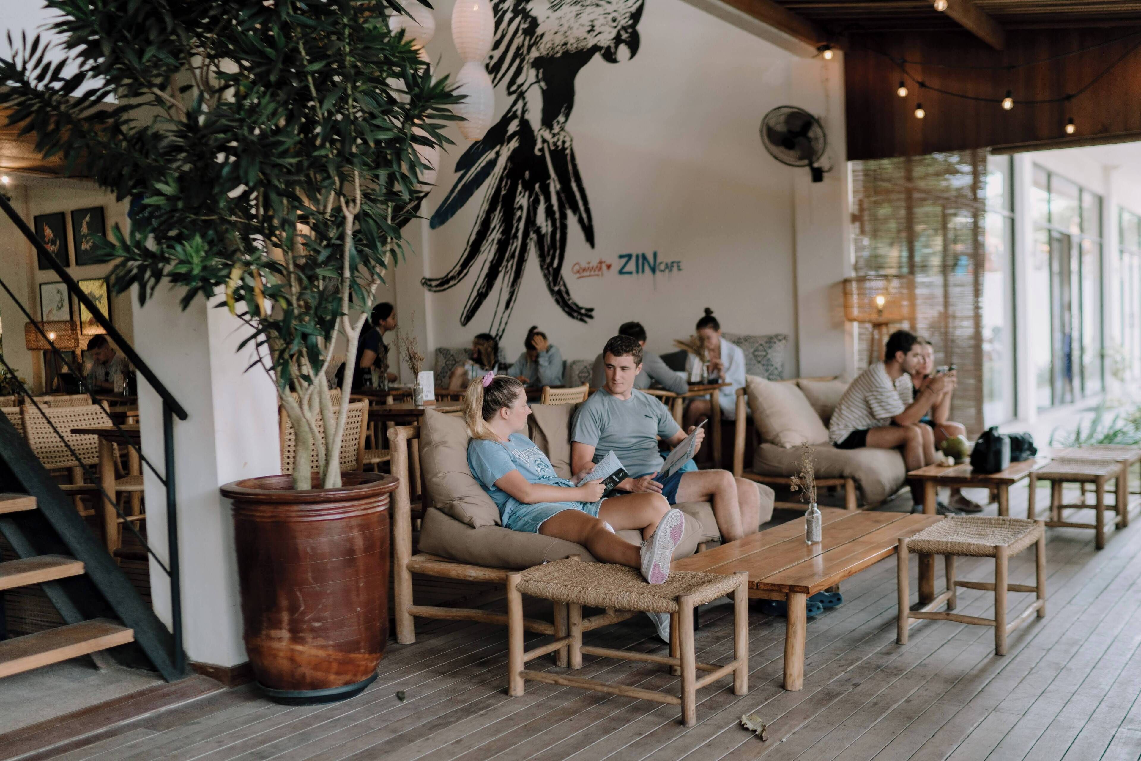 A cozy cafe interior with wooden furniture, potted plants, and a mural on the wall.