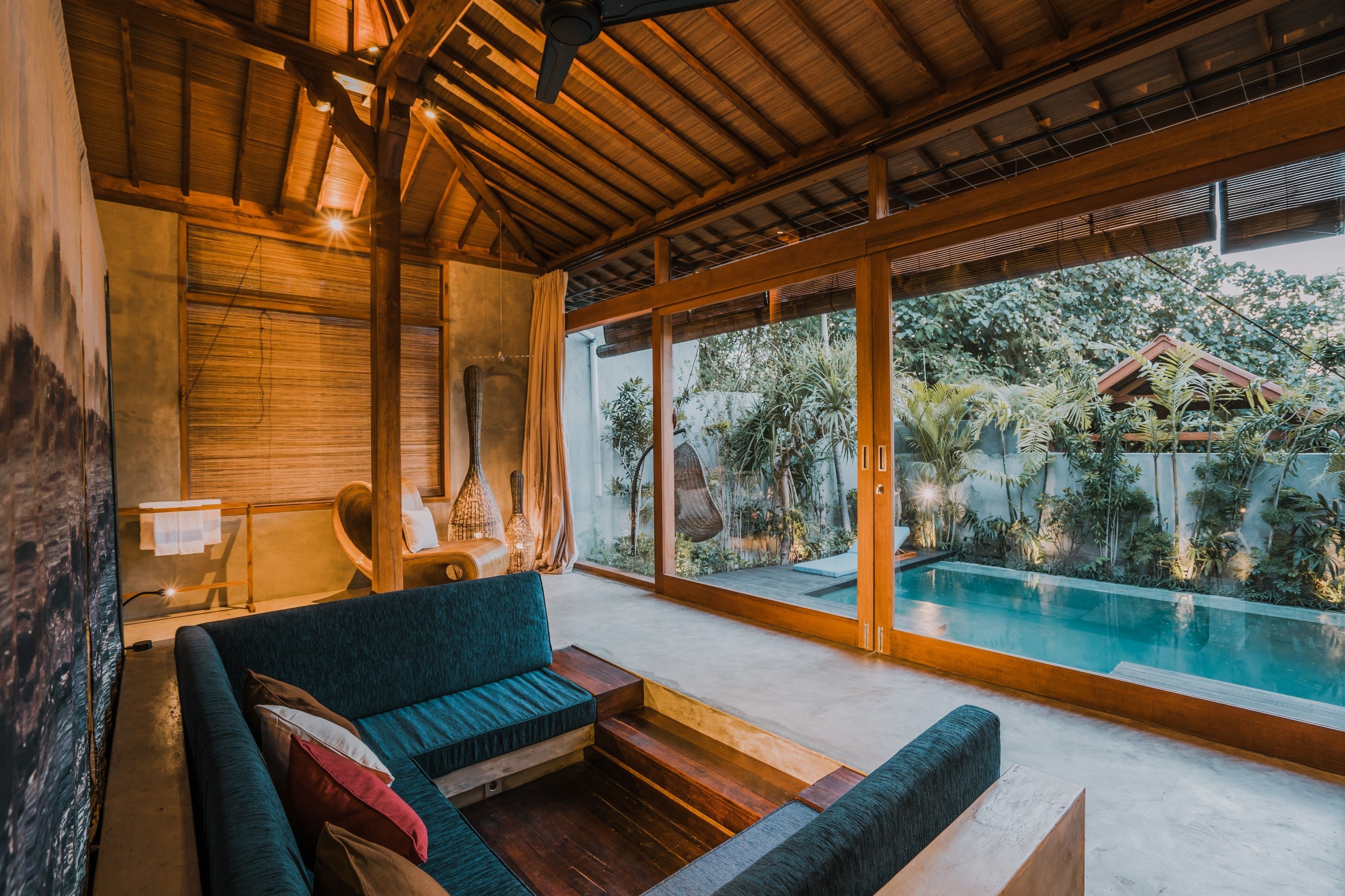 A modern interior with a wooden ceiling, a blue sofa, and a view of an outdoor swimming pool.