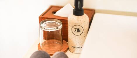A wooden tray with a glass of water, a bottle of body lotion, and a pair of gray slippers.