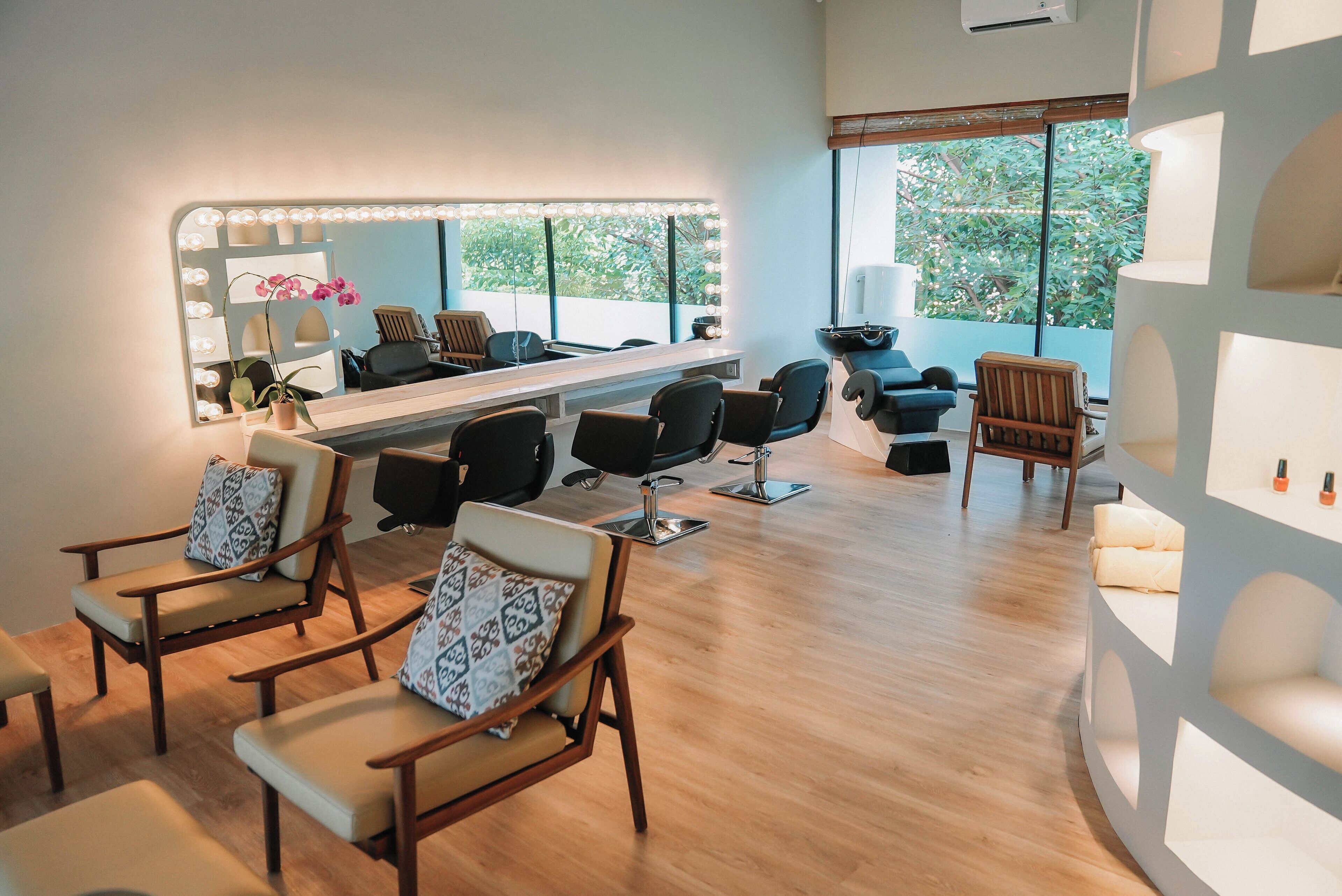 A salon with a large mirror, multiple chairs, and a view of greenery outside.