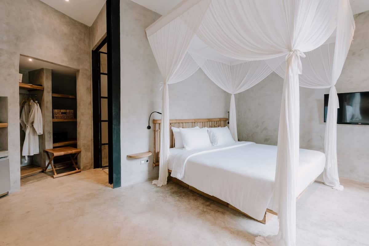 Une chambre à coucher avec un lit à baldaquin, une tête de lit en bois, une table de chevet, un banc, une armoire et un téléviseur fixé au mur.