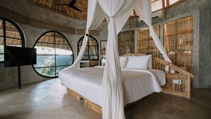 Une chambre spacieuse avec un grand lit, une tête de lit en bois et un lit à baldaquin. De grandes fenêtres à arc donnent sur un paysage verdoyant.