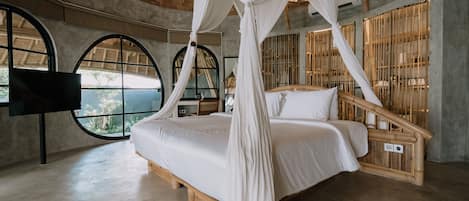 A spacious bedroom with a large bed, a wooden headboard, and a canopy bed. There are large windows with arched tops and a view of greenery outside.