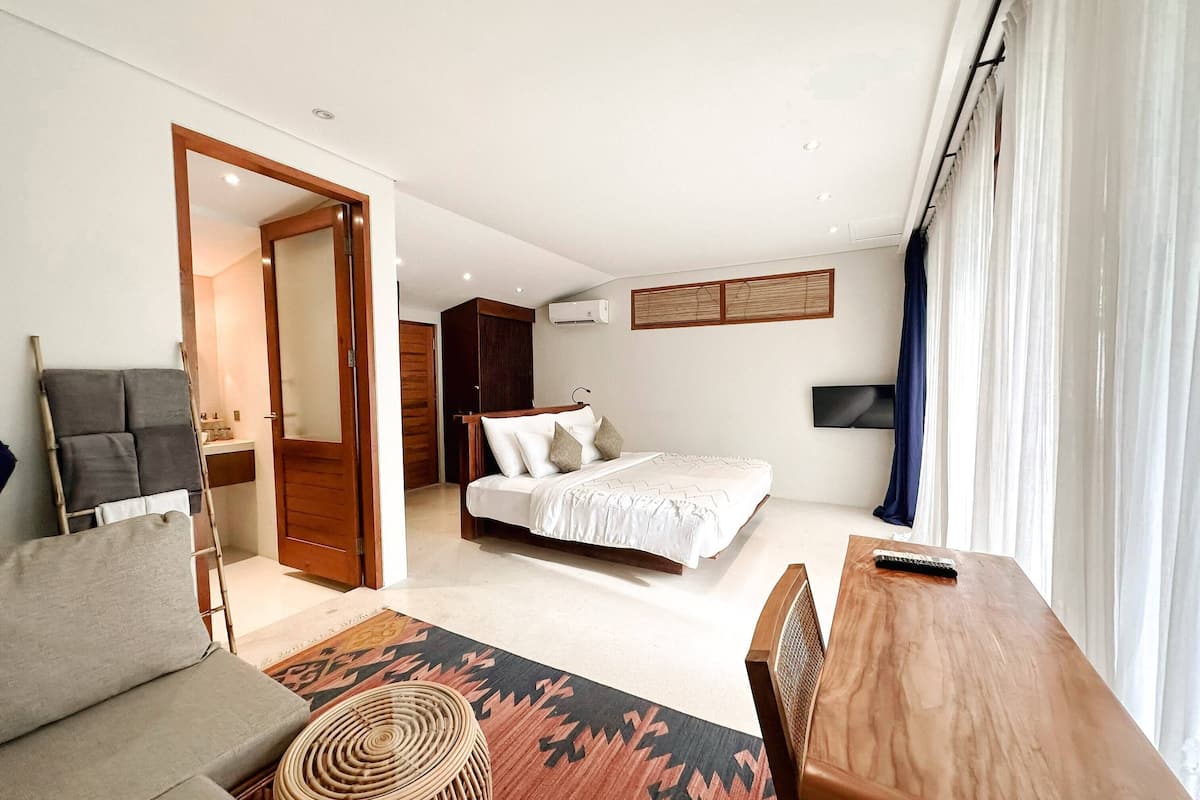 Une chambre d’hôtel avec un lit, un bureau en bois, un canapé, une petite table ronde et un miroir.