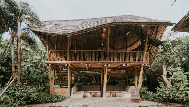 Une structure en bois avec un toit de chaume, une piscine et un espace détente avec des coussins.