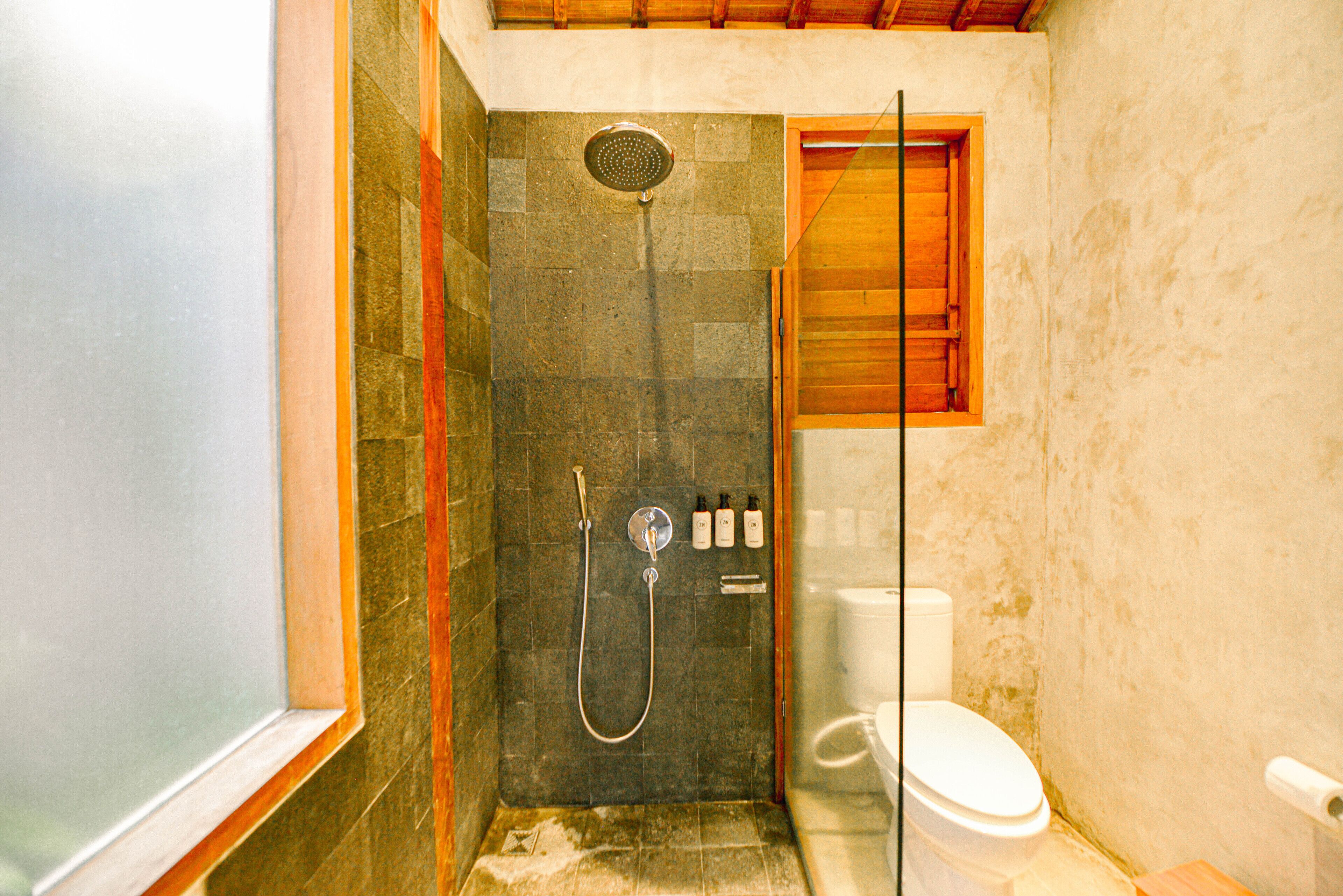 Un espacio de ducha pequeño y cerrado con puerta de cristal, alcachofa de ducha y un inodoro.