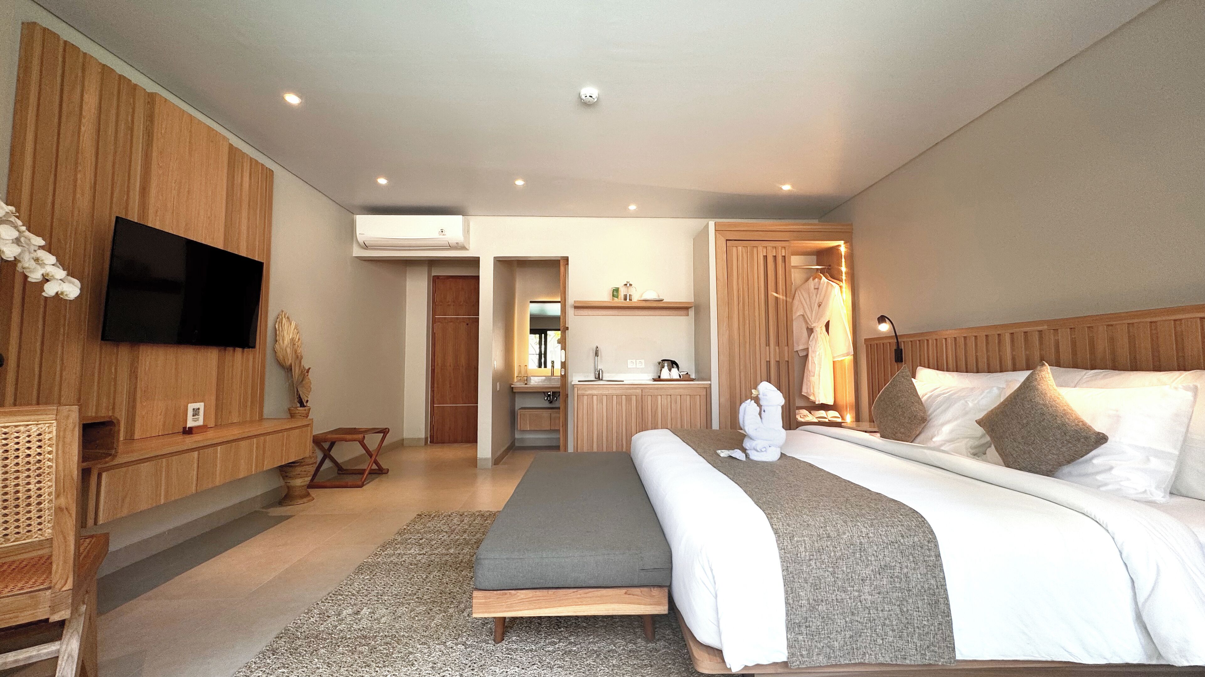 A modern hotel room with a large bed, a television, a kitchenette, and a bathroom.