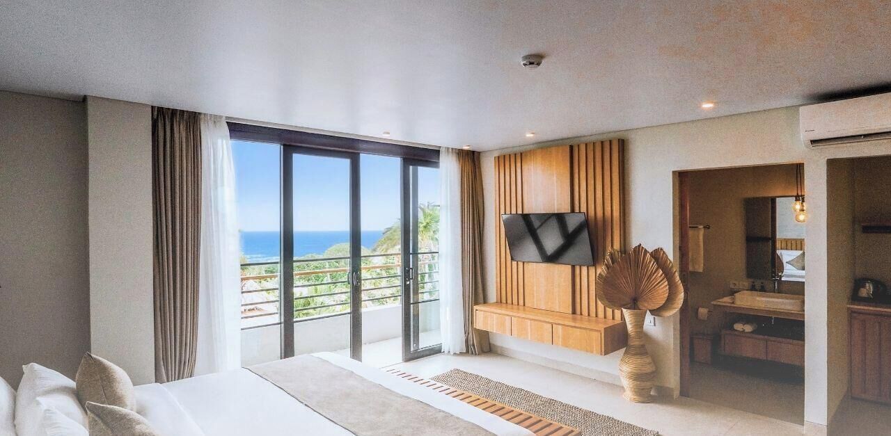 A hotel room with a large sliding glass door leading to a balcony with a view of the ocean.