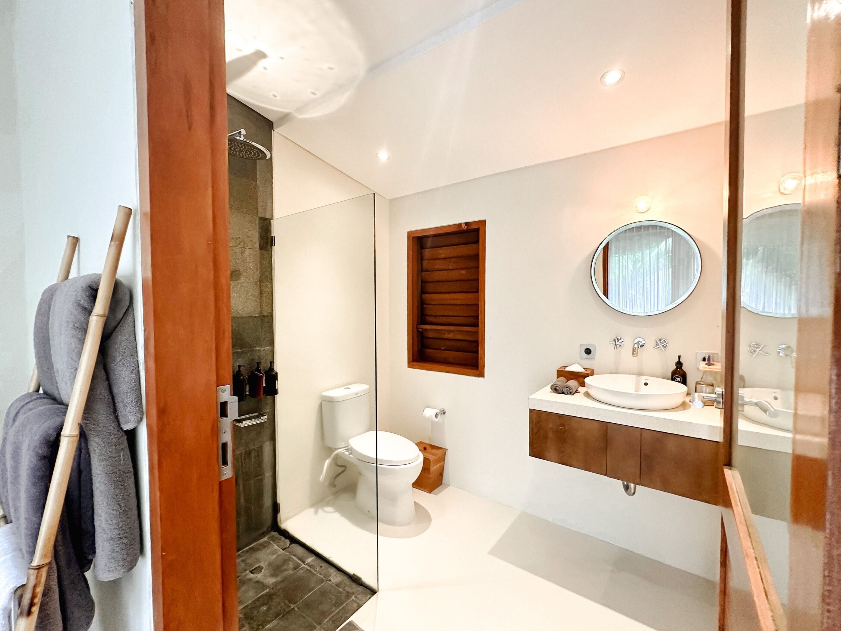 A modern bathroom with a toilet, sink, and shower. There are towels and toiletries visible.