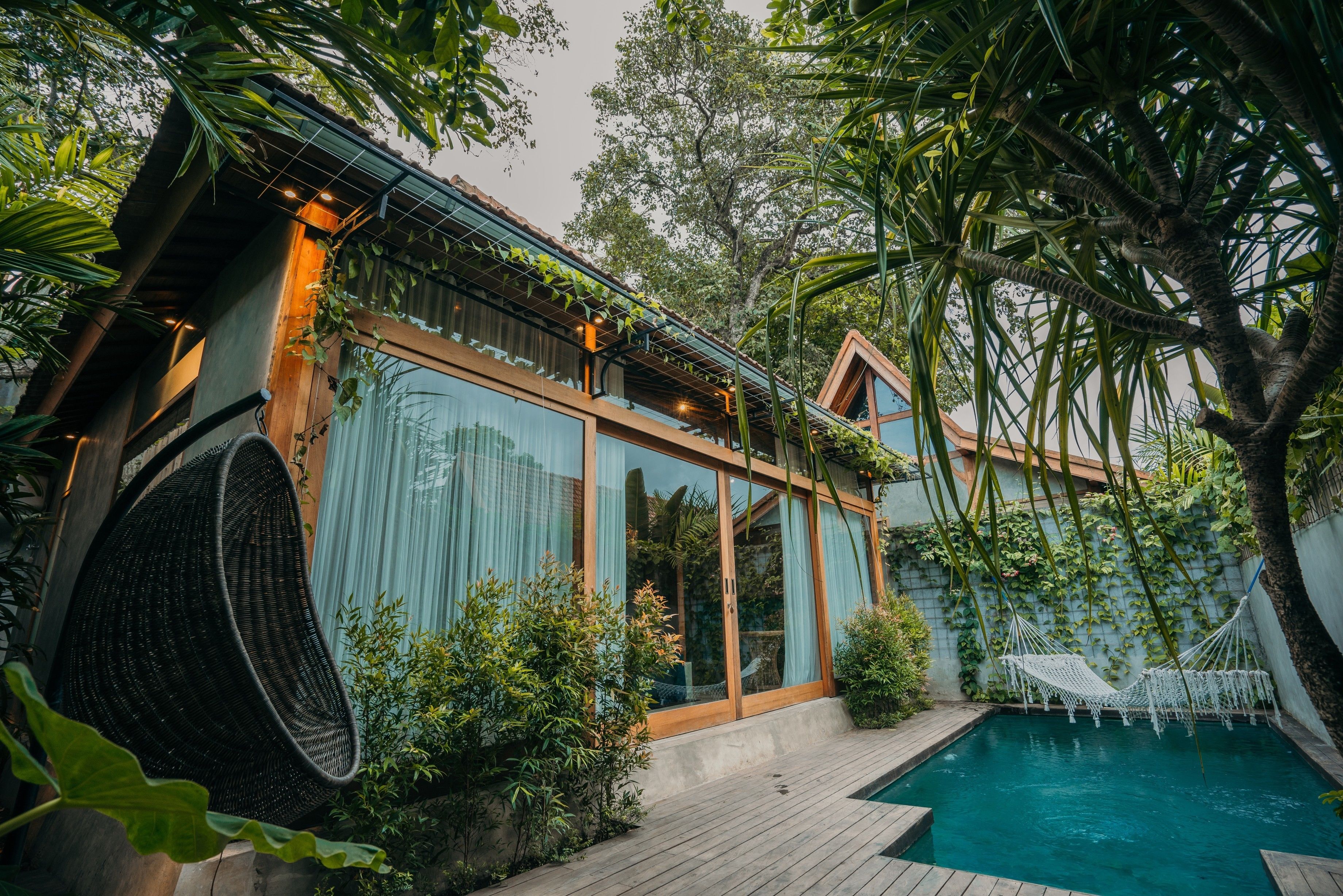 A modern house with a pool, large windows, and a hammock.