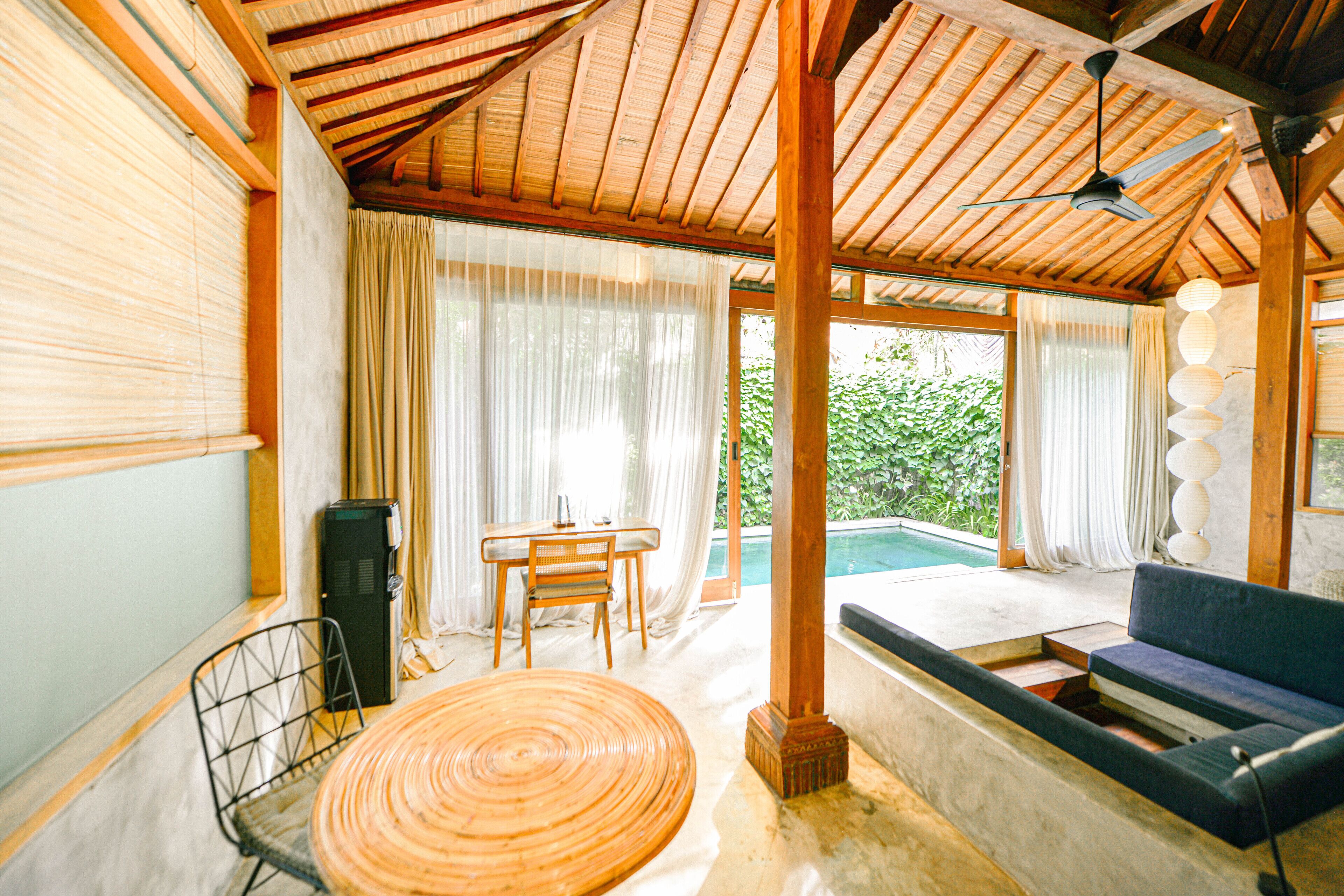 A room with a wooden ceiling, a pool, a sofa, a table with chairs, and a TV.